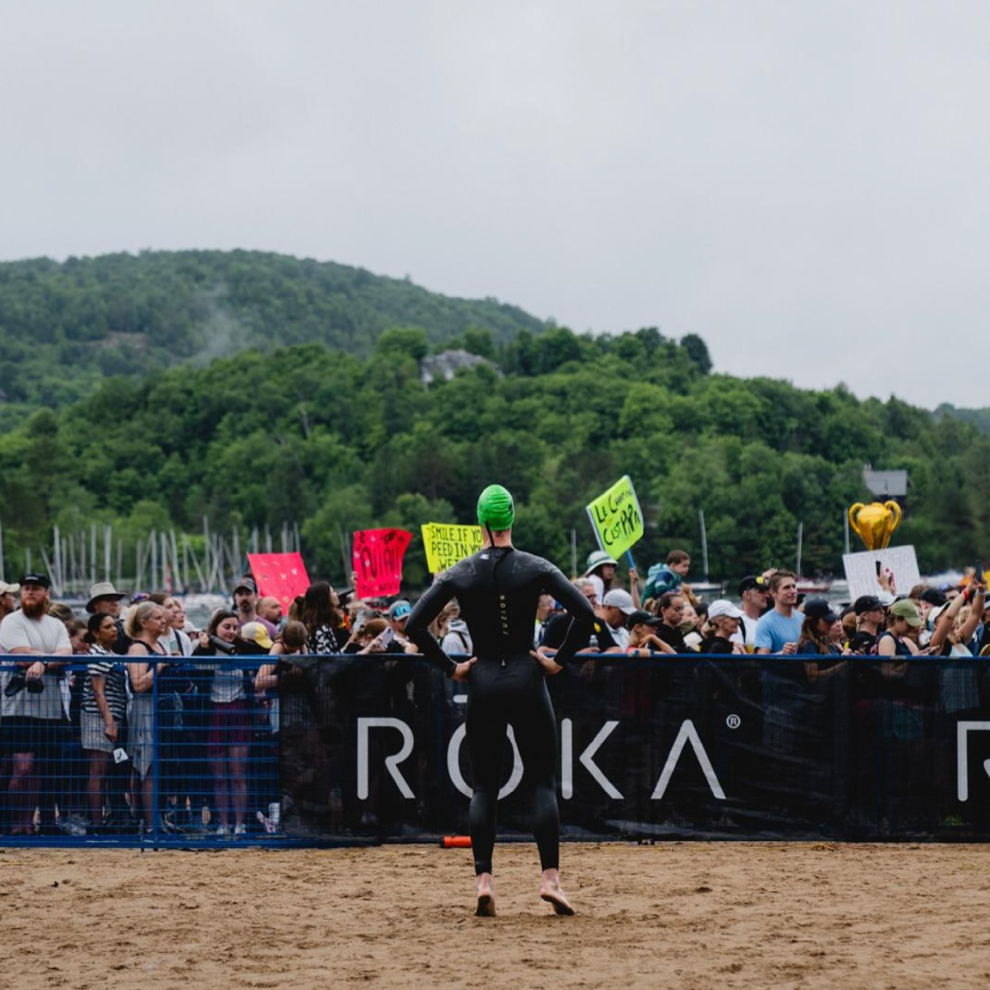 Athlete in a wetsuit standing on a beach with a crowd and Roka branding in the background, representing healthy active lifestyle and endurance sports – ero Evergreen supplement lifestyle photography.