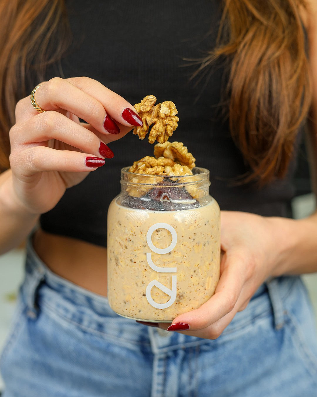Hand topping a glass jar of ero overnight oats with walnuts