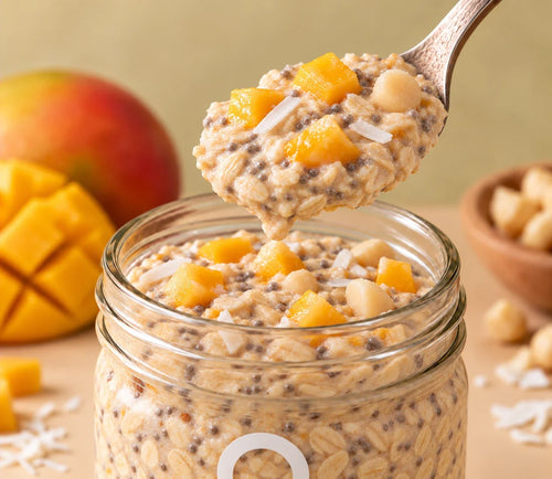 Spoonful of ero Mango, Macadamia & Coconut overnight oats being lifted from a glass jar—bright, tropical, high-protein breakfast.