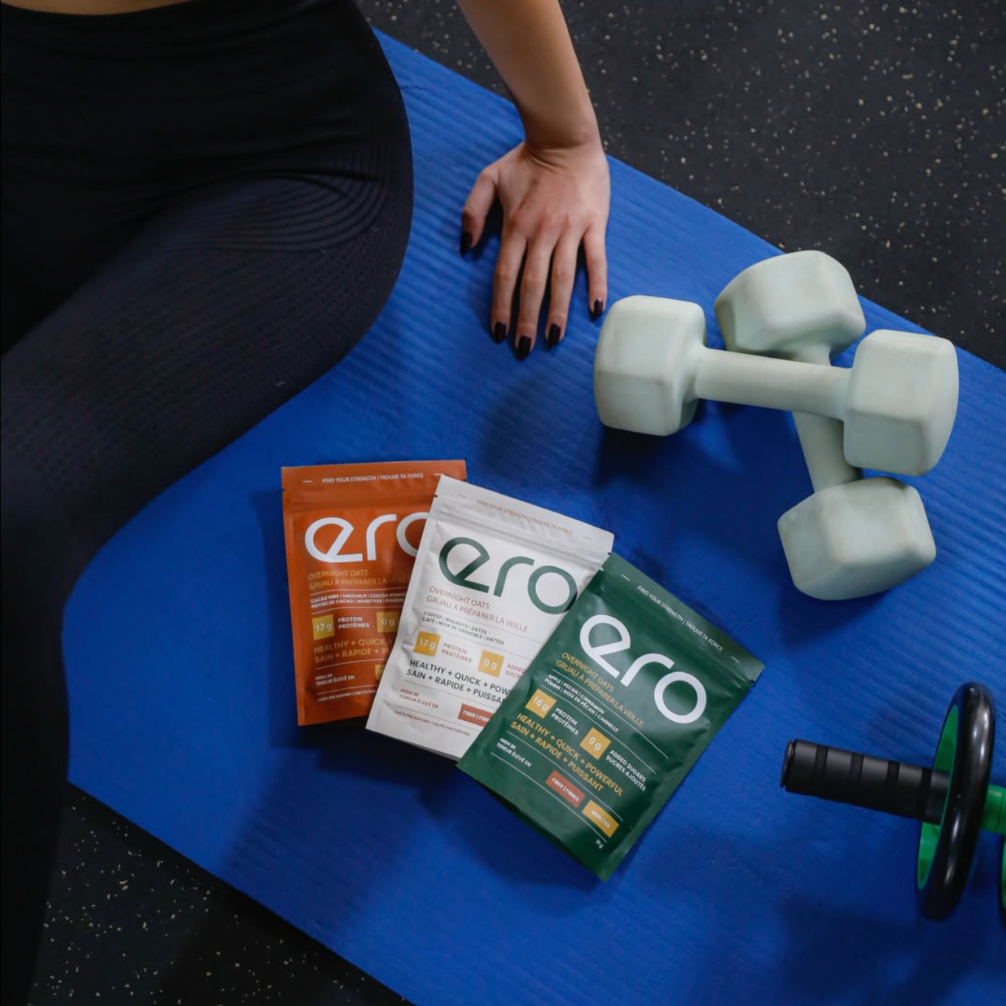 Ero supplements on a blue exercise mat with dumbbells and an ab wheel in the background, representing fitness, strength training, and active lifestyle.