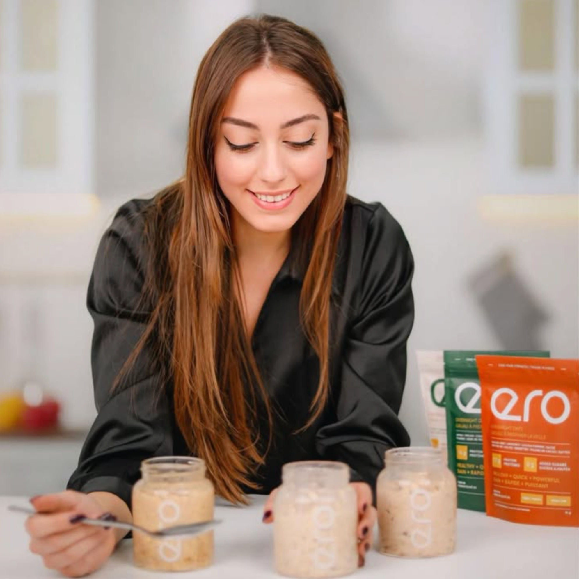 Woman sitting at a kitchen table with glass jars and Ero supplements, highlighting healthy lifestyle, product use, and modern wellness routines.